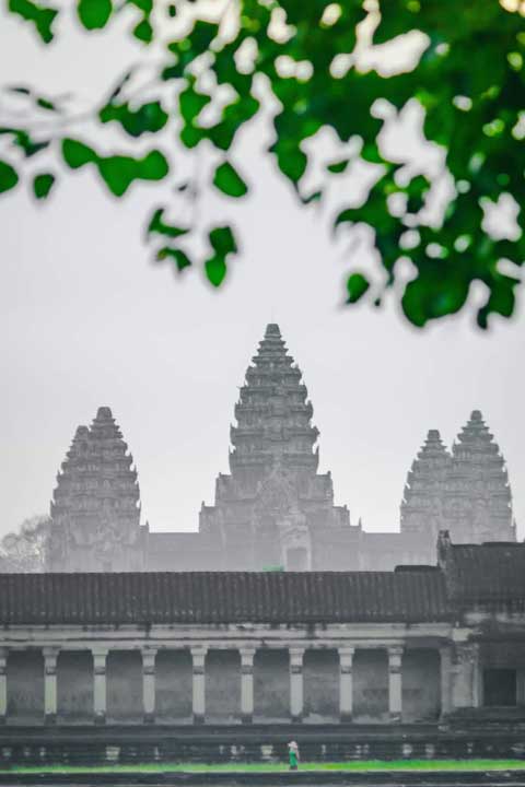 Angkor Wat temple in Cambodia, partially obscured by foliage, during the green season.