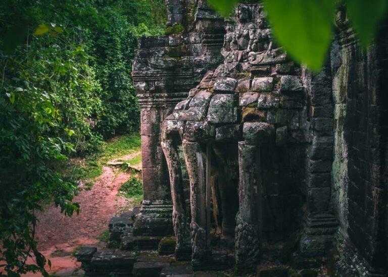 Landscape view of ancient stone carvings at Khmoch Gate (Gate of the Dead), framed by lush greenery, showcasing Cambodia’s rich history and natural beauty during the green season.